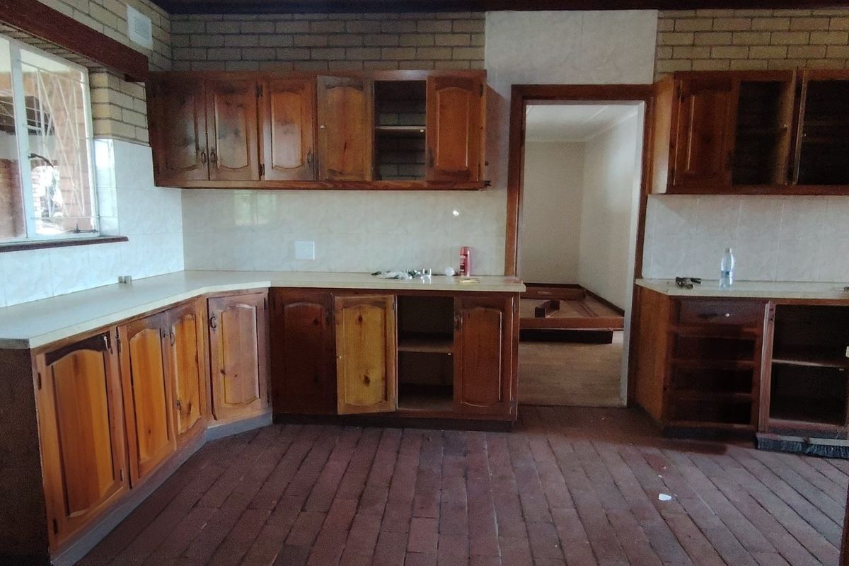 A dated kitchen featuring wooden cabinetry, brick walls, and timber ceilings, currently empty and in need of renovation to modernize the space.