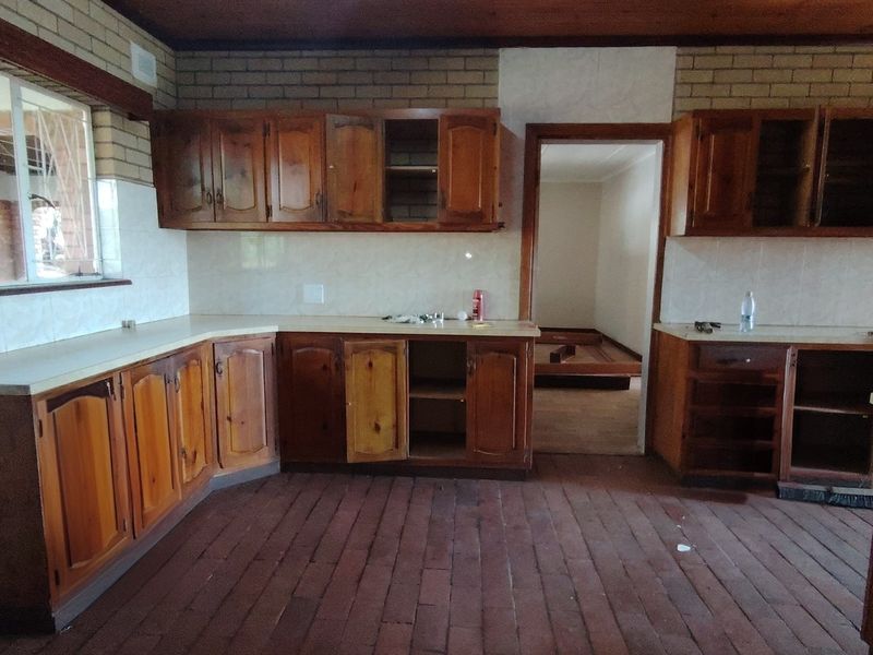 A dated kitchen featuring wooden cabinetry, brick walls, and timber ceilings, currently empty and in need of renovation to modernize the space.