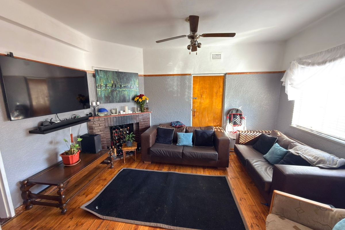 A living room featuring hardwood flooring, a brick fireplace, and a ceiling fan, with a classic layout and traditional architectural details.