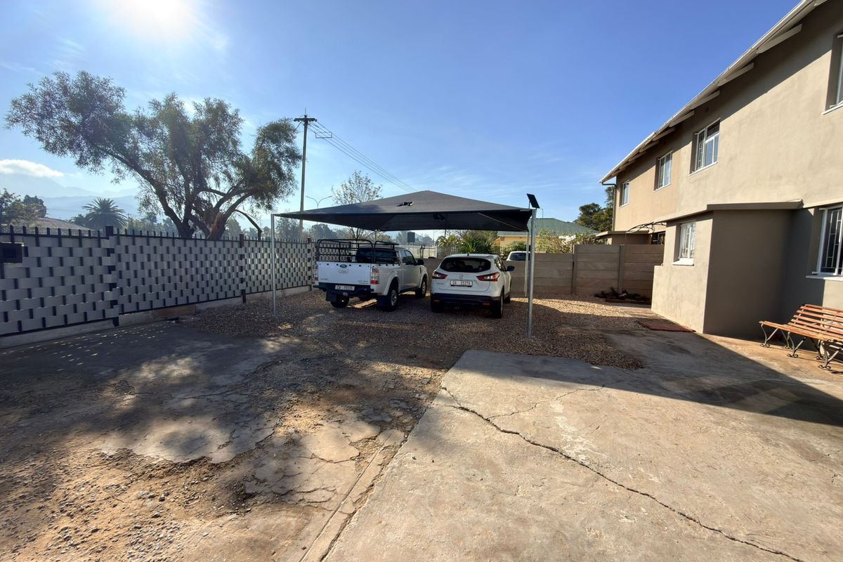 Rear exterior area featuring a gravel driveway, a shade-cloth carport, and a precast concrete boundary wall.