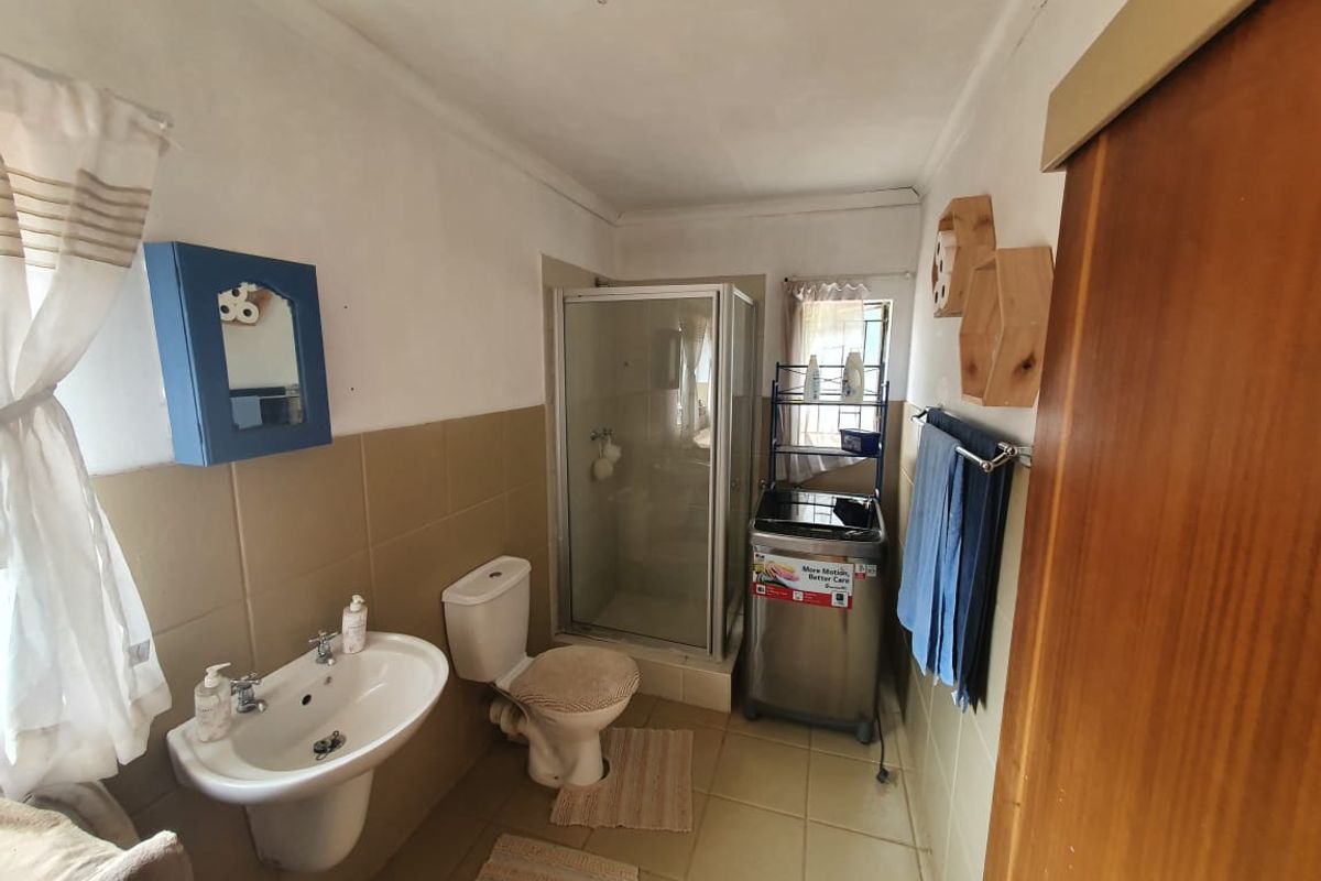 A functional bathroom featuring a pedestal basin, toilet, and a glass-enclosed shower with neutral wall tiling.