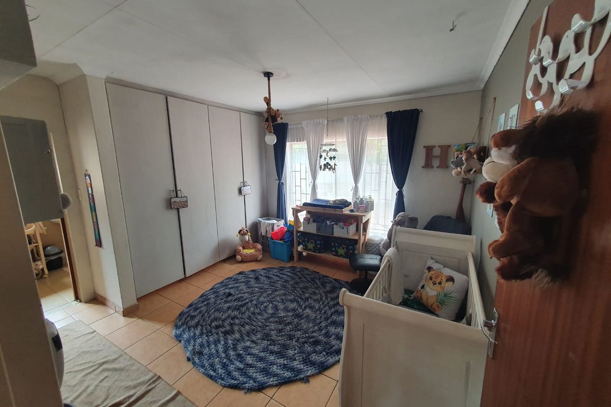 A functional bedroom featuring built-in cupboards, tiled flooring, and security bars on the window, currently utilized as a nursery.