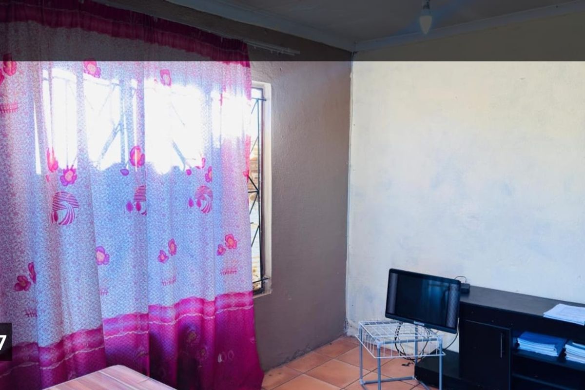 A living room area featuring tiled flooring, security bars on the window, and basic wall finishes.