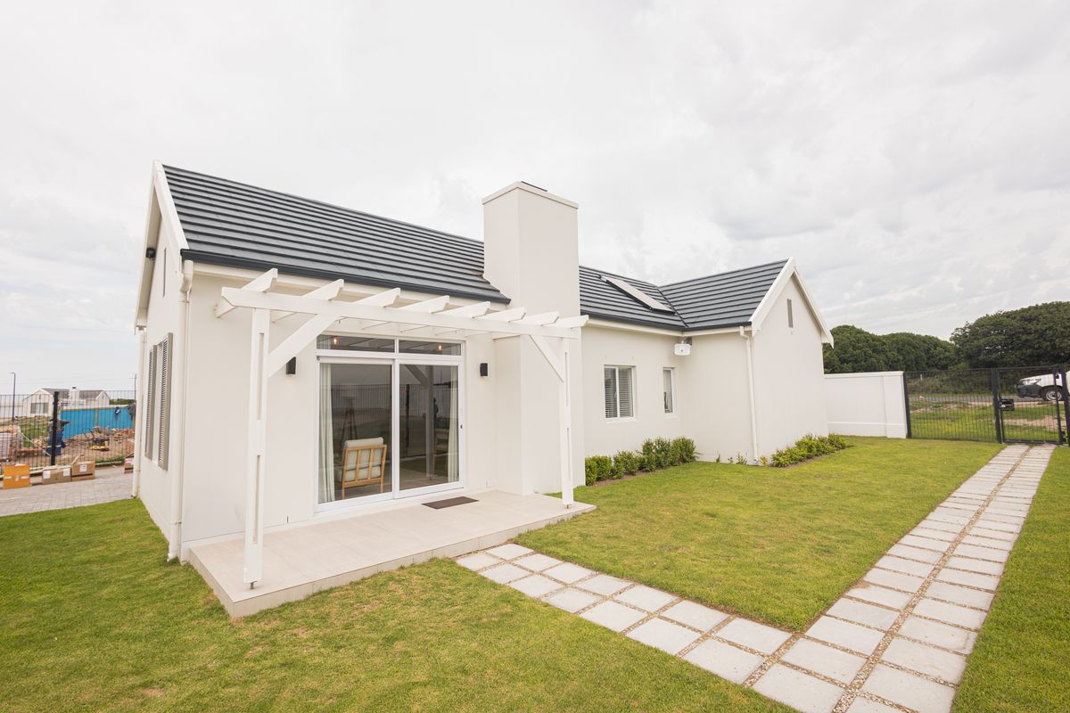 Rear view of a modern house featuring a tiled roof, chimney, white pergola over a tiled patio, and a well-maintained lawn with a paved walkway.