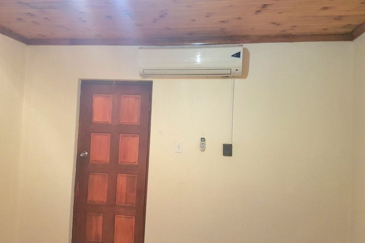 A simple bedroom featuring a timber ceiling, a wall-mounted split-system air conditioner, and a classic panelled timber door.
