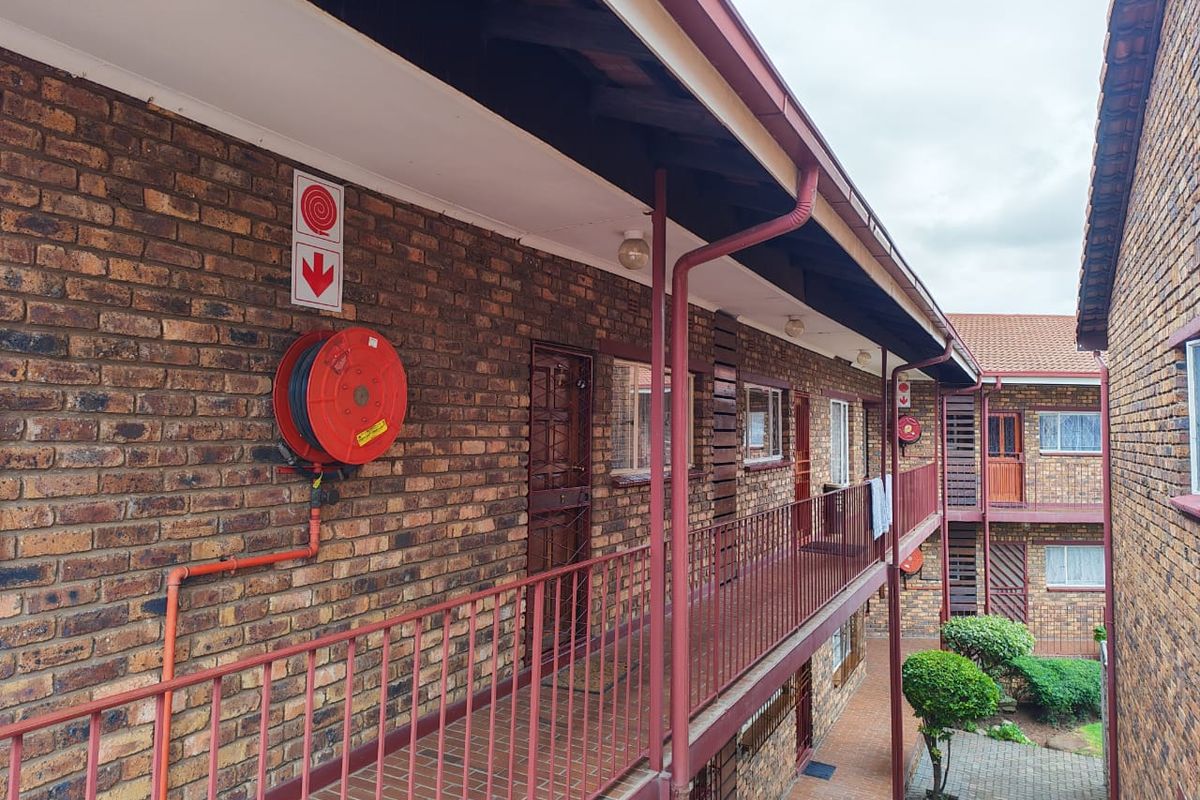 Exterior view of an apartment complex featuring a brick facade, covered walkway with metal railings, and fire safety equipment.
