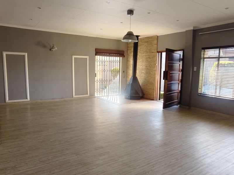 Spacious living area featuring laminate flooring, a freestanding fireplace, and large windows with venetian blinds, offering a bright and open layout.