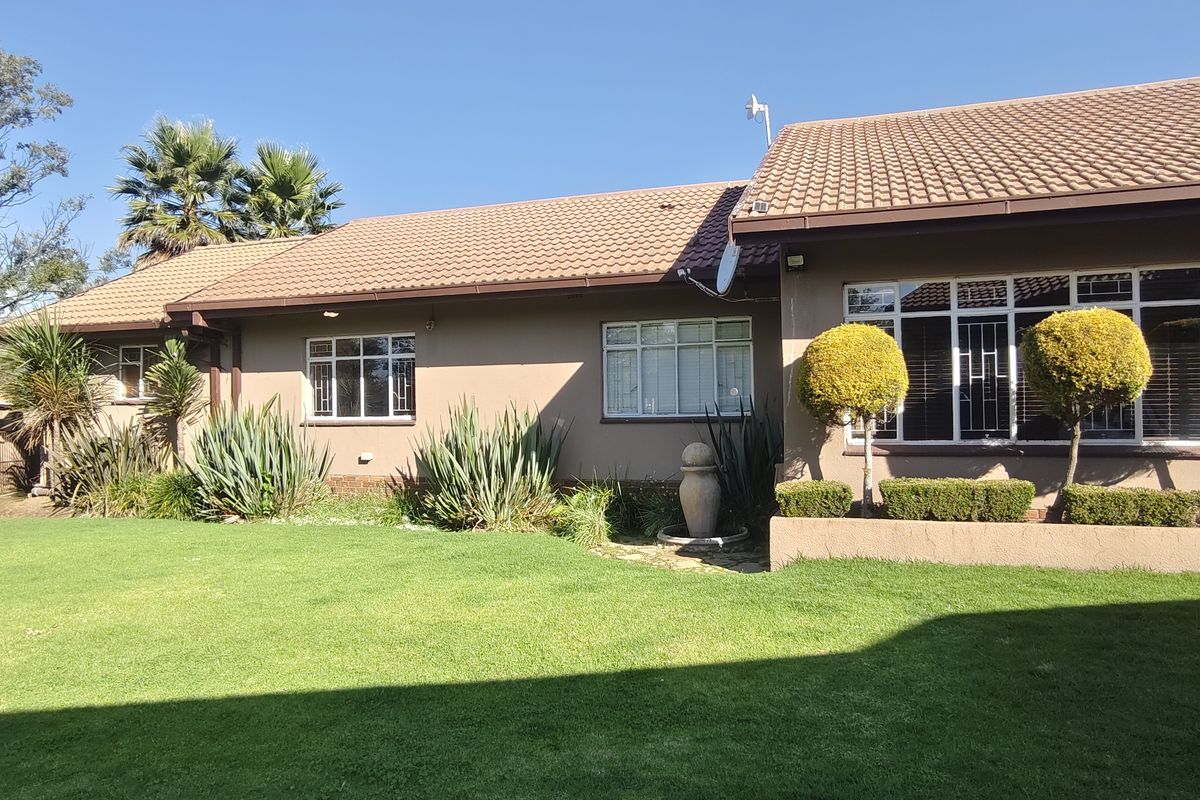 A well-maintained rear exterior view of the house featuring a tiled roof, landscaped garden, and secure aluminium-framed windows.