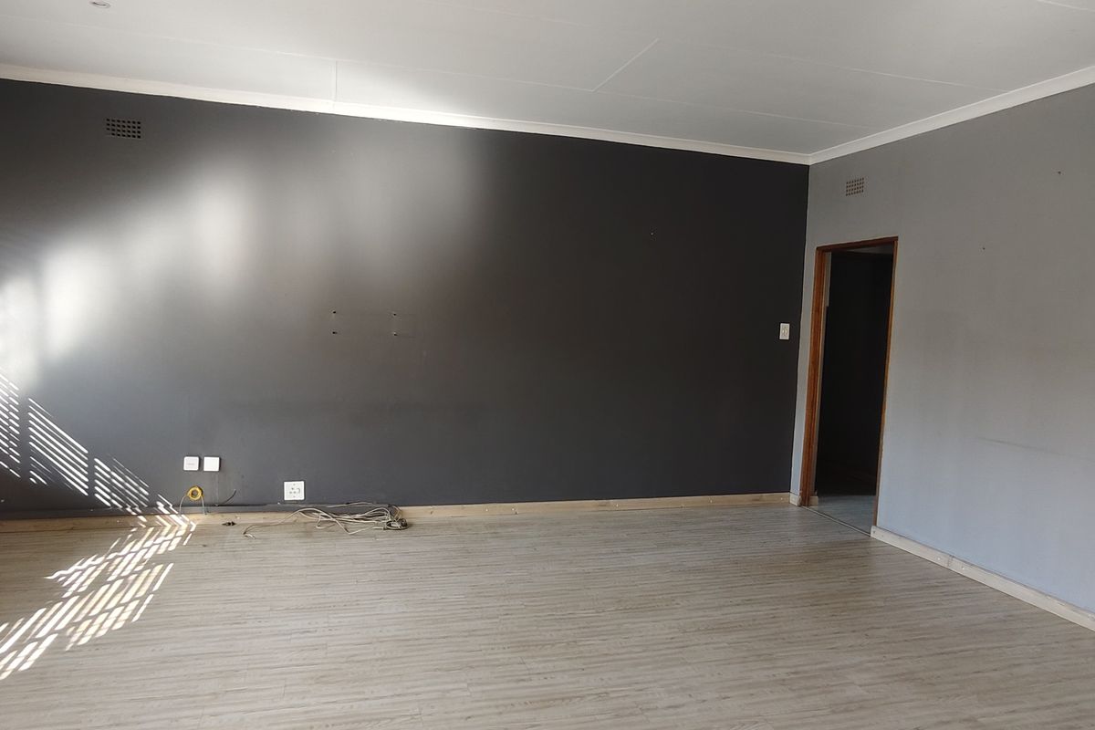 An empty living room featuring laminate flooring, neutral grey walls, and natural light through large windows with fitted blinds.