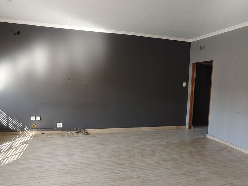 An empty living room featuring laminate flooring, neutral grey walls, and natural light through large windows with fitted blinds.