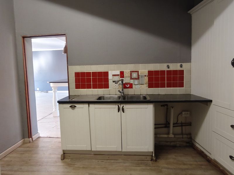 A functional kitchen area featuring white cabinetry, a double sink, and a red tiled splashback, with an open doorway leading to an adjacent room.