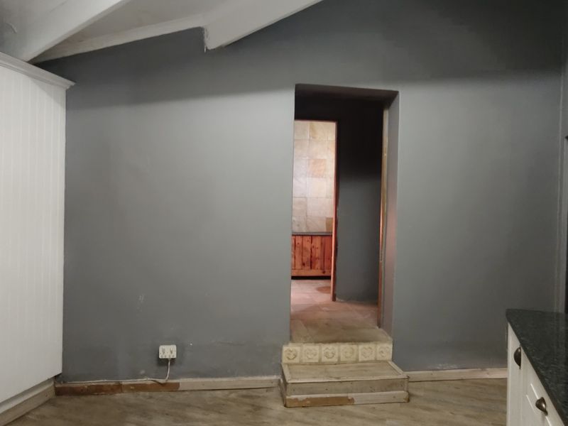 A kitchen area featuring built-in white cabinetry, dark stone countertops, and a raised doorway leading to an adjacent tiled space.