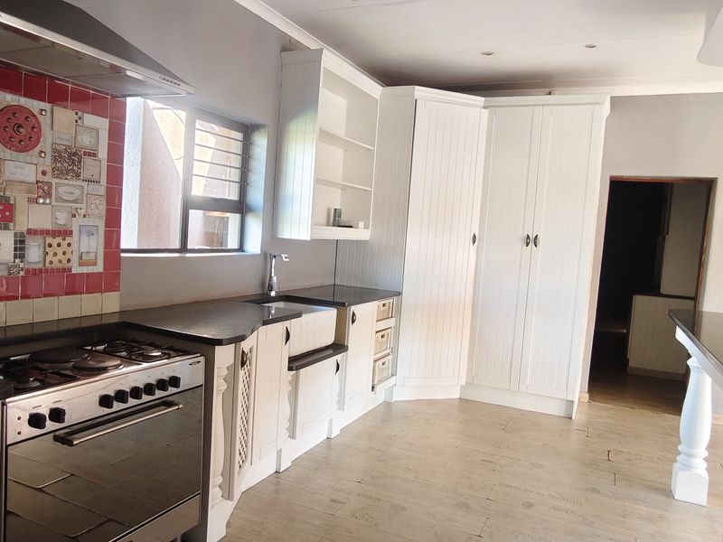 A bright kitchen featuring white cabinetry, stone countertops, a farmhouse sink, and a gas stove with a decorative tiled splashback.