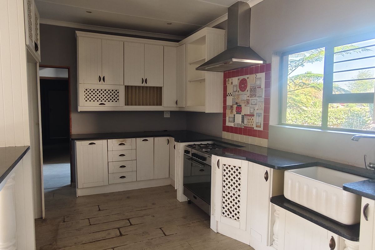 A bright kitchen featuring white cabinetry, granite countertops, a farmhouse sink, and a gas stove with a stainless steel extractor fan.