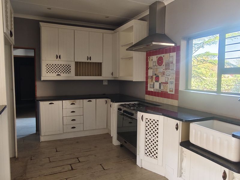 A bright kitchen featuring white cabinetry, granite countertops, a farmhouse sink, and a gas stove with a stainless steel extractor fan.
