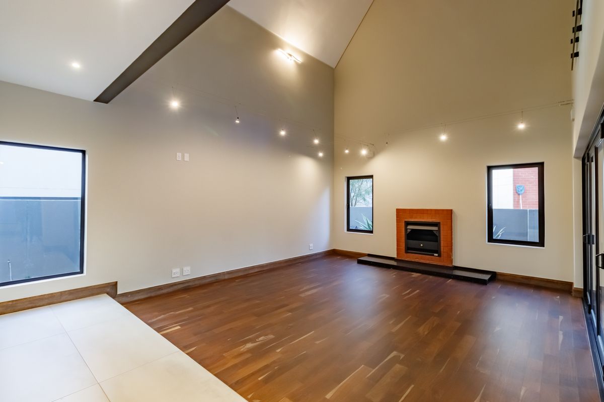 Spacious living room featuring a vaulted ceiling, exposed beam, hardwood flooring, and a built-in fireplace with a hearth.