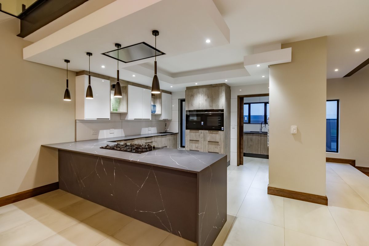 Modern kitchen featuring a large stone island with integrated gas hob, sleek cabinetry, built-in double ovens, and recessed lighting, with an adjacent scullery area.