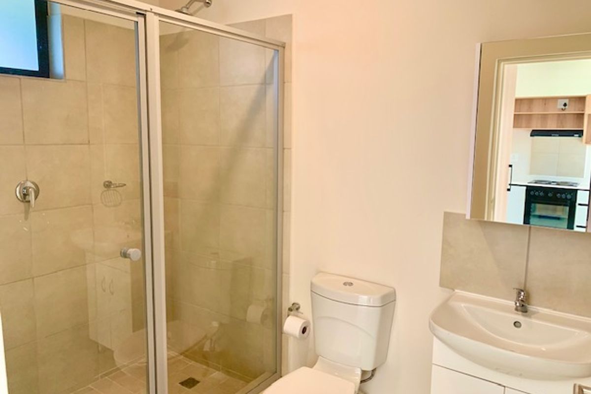 A functional bathroom featuring a glass-enclosed shower, a white ceramic toilet, and a vanity basin with storage cabinetry.