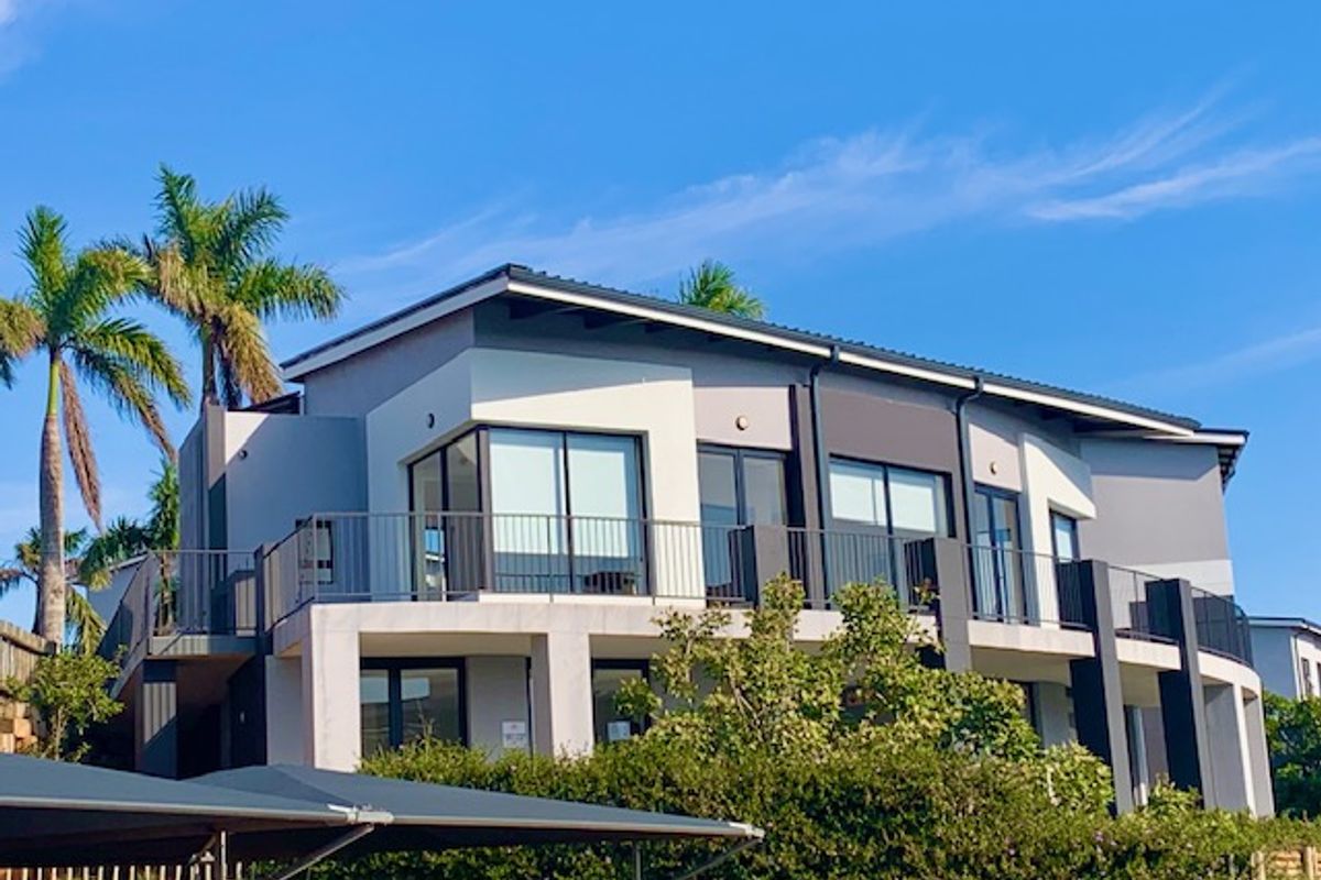 A modern multi-level apartment building exterior featuring contemporary grey and white facade finishes, large glass sliding doors, and private balconies with metal railings.