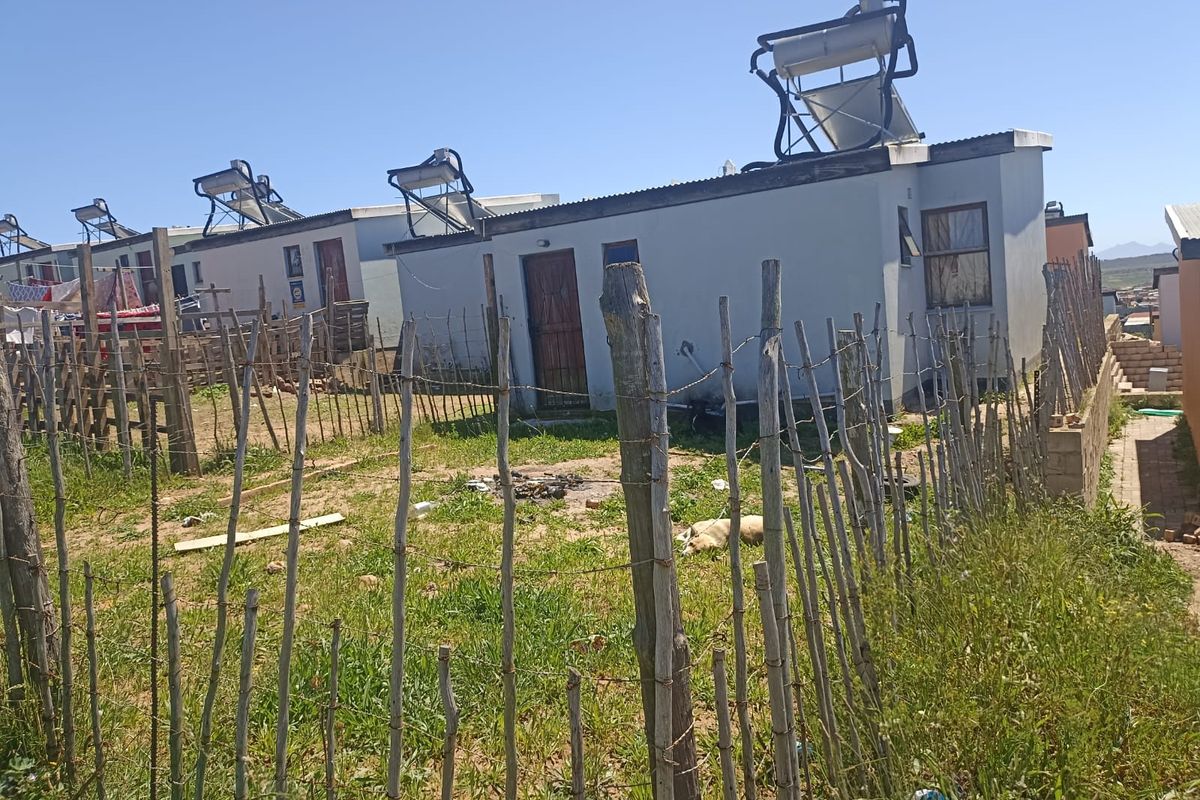 Rear view of residential units featuring solar water heating systems and basic perimeter fencing.
