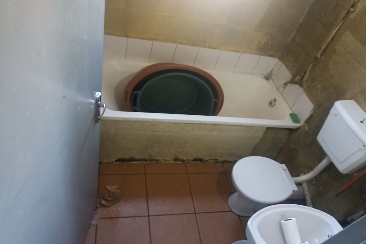 A small bathroom featuring a bathtub, toilet, and pedestal basin, currently requiring significant renovation and repair to wall finishes and fixtures.