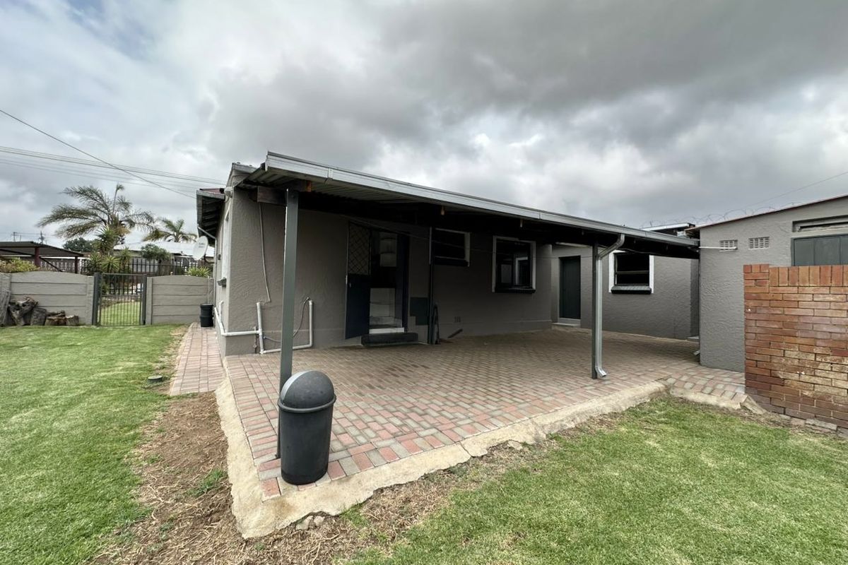 Rear view of the property featuring a covered paved patio area, brick boundary wall, and surrounding lawn space.