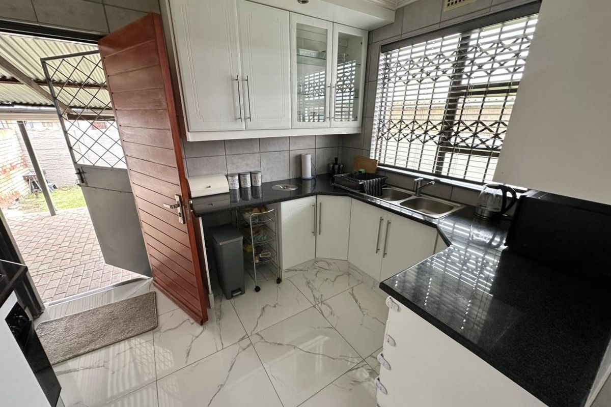 A well-maintained kitchen featuring white cabinetry, dark granite countertops, double stainless steel sink, and modern marble-look floor tiles with direct outdoor access.
