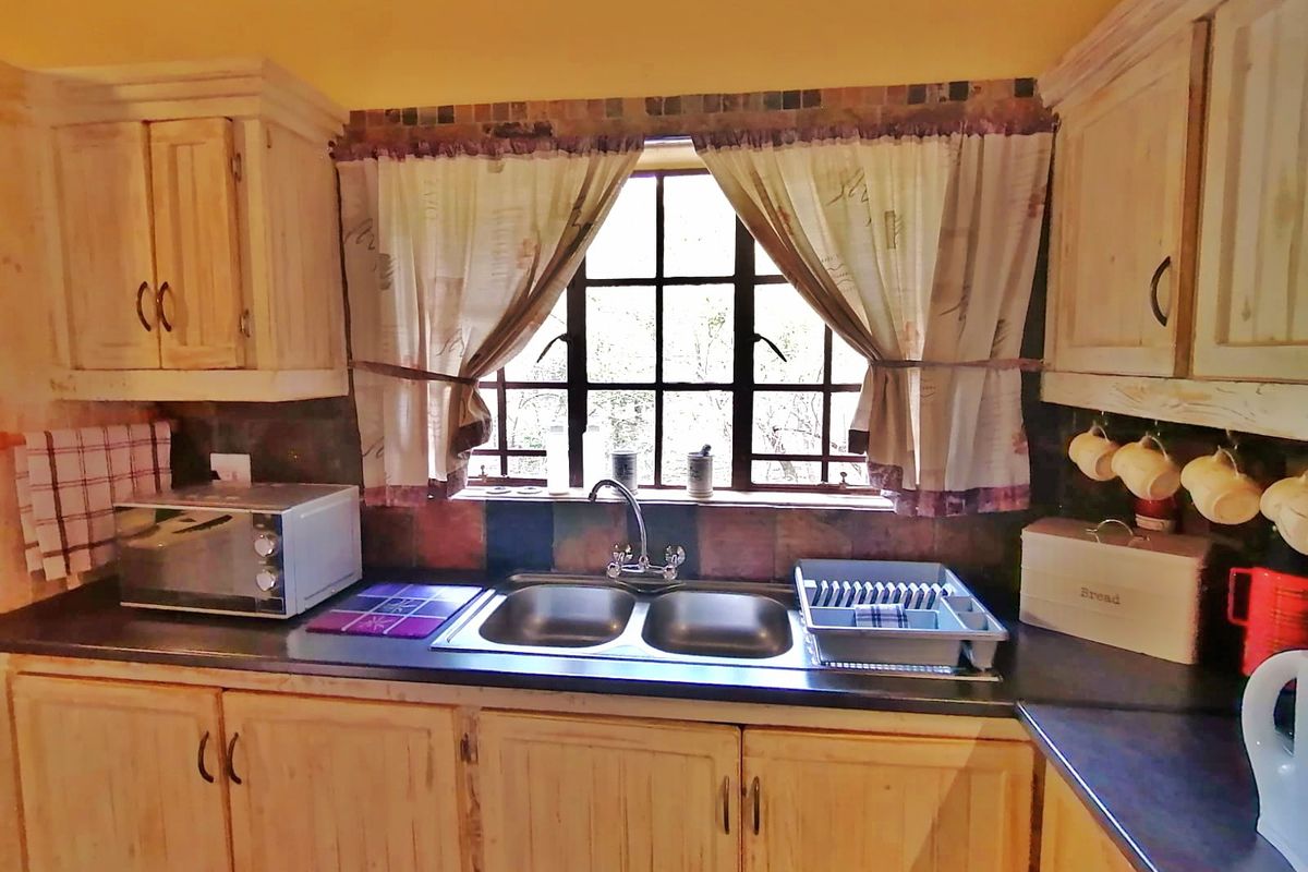 A functional kitchen featuring wooden cabinetry, a double basin sink, and a tiled splashback, providing a classic, lived-in aesthetic.
