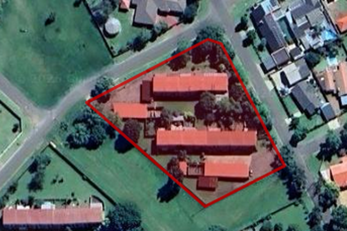 An aerial view of the apartment complex property, highlighting the building layout, roof structure, and surrounding grounds.