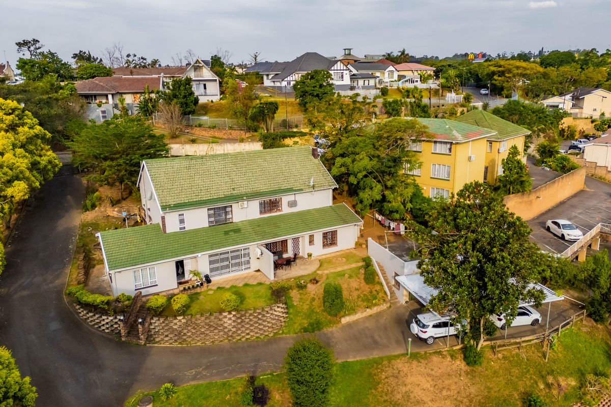 Aerial view of a townhouse property featuring a green tiled roof, terraced garden, retaining walls, and a paved driveway with a carport.