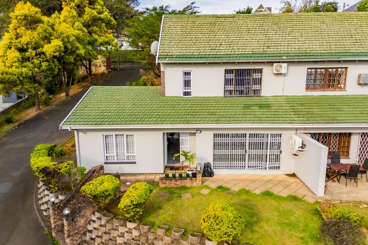 Rear view of the townhouse featuring a paved patio, green tiled roof, security gates, and a landscaped garden with a retaining wall.
