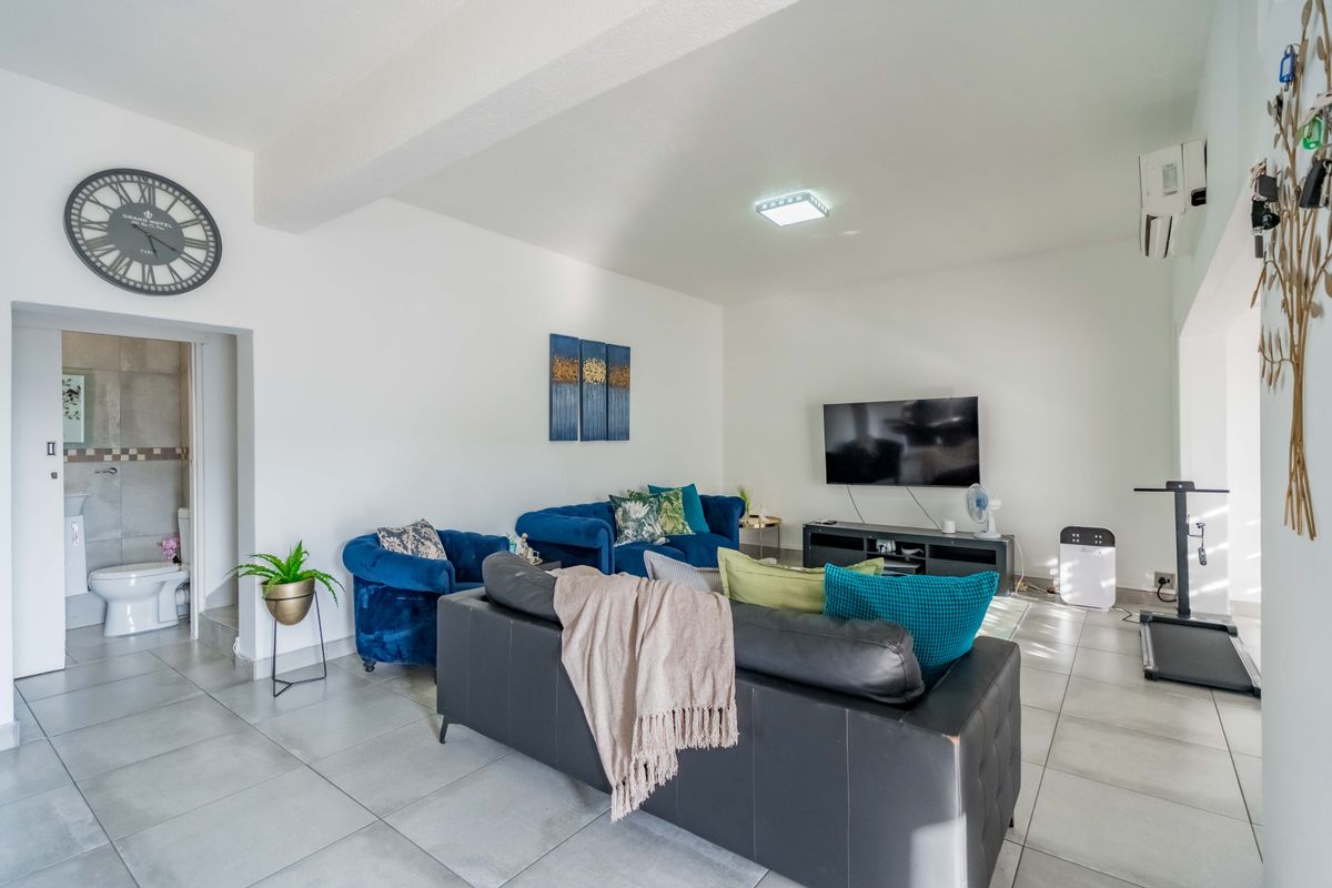 Spacious living room featuring neutral tiled flooring, a wall-mounted air conditioning unit, and direct access to an adjacent bathroom.