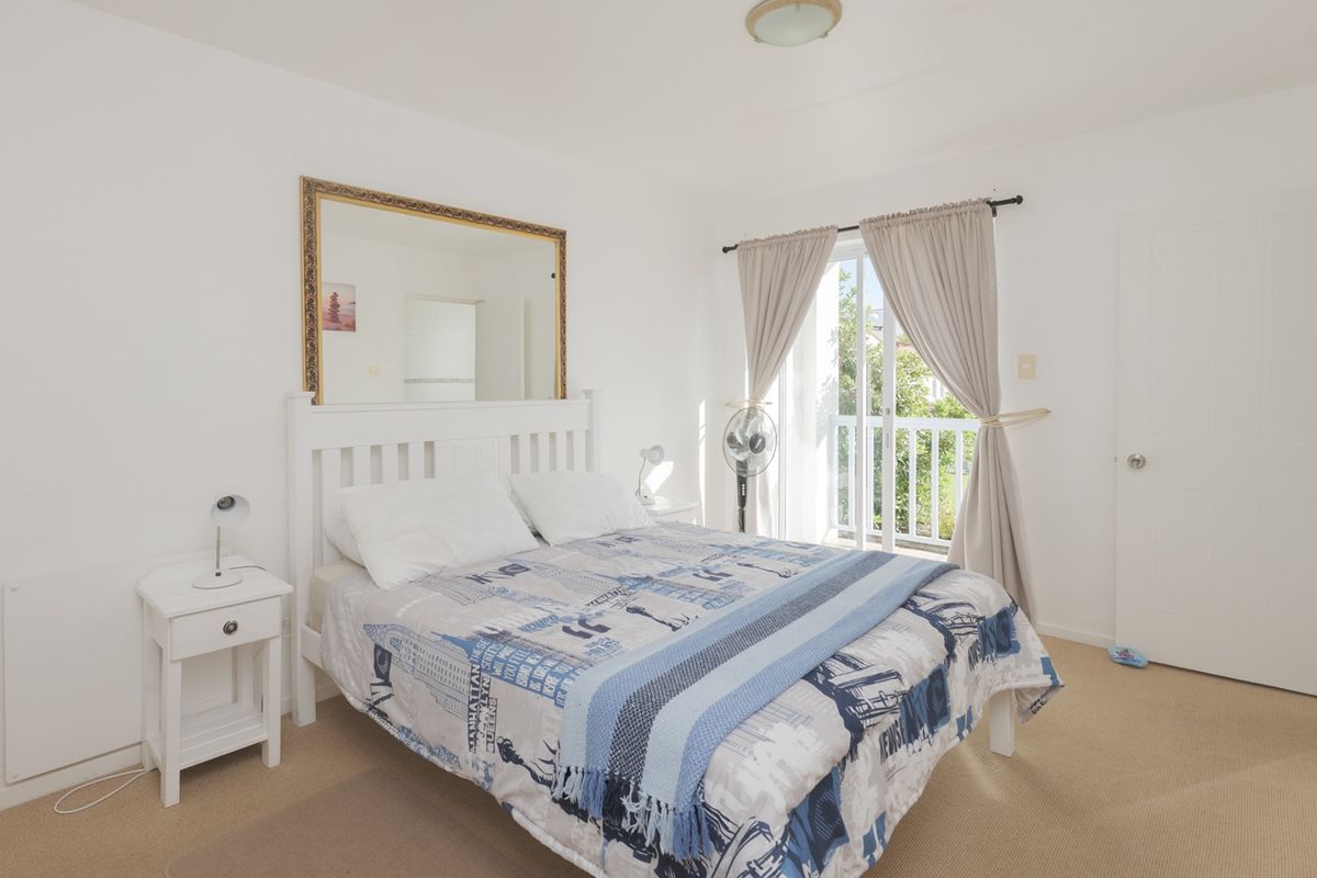 A bright bedroom featuring carpet flooring, a ceiling light fixture, and a sliding glass door providing direct access to a private balcony.