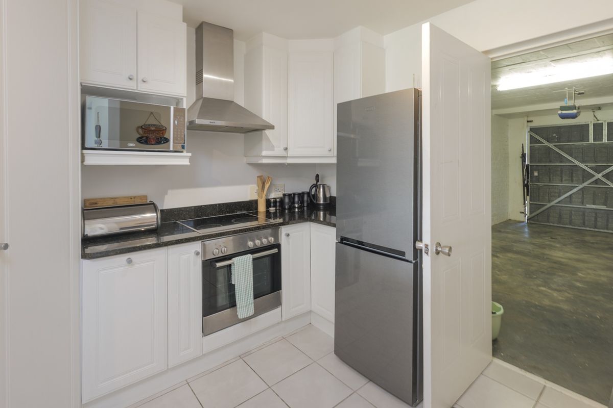Compact kitchen featuring white cabinetry, black granite countertops, stainless steel appliances, and tiled flooring, with direct access to the garage area.