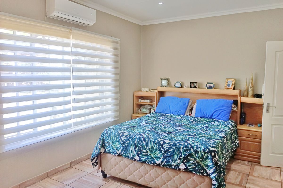 A well-maintained bedroom featuring tiled flooring, recessed downlighting, and a wall-mounted split-system air conditioning unit.