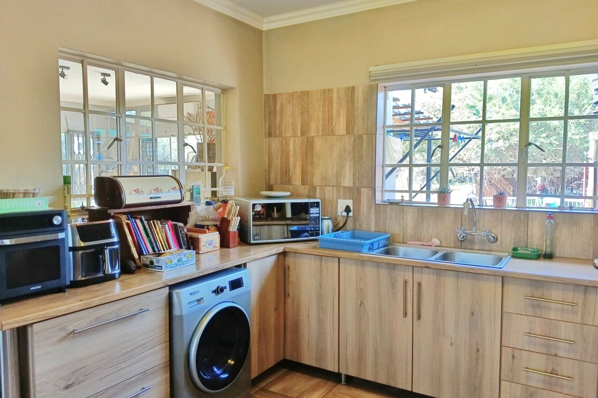 A functional kitchen featuring wood-look laminate cabinetry, a double stainless steel sink, tiled splashbacks, and a dedicated space for a washing machine.