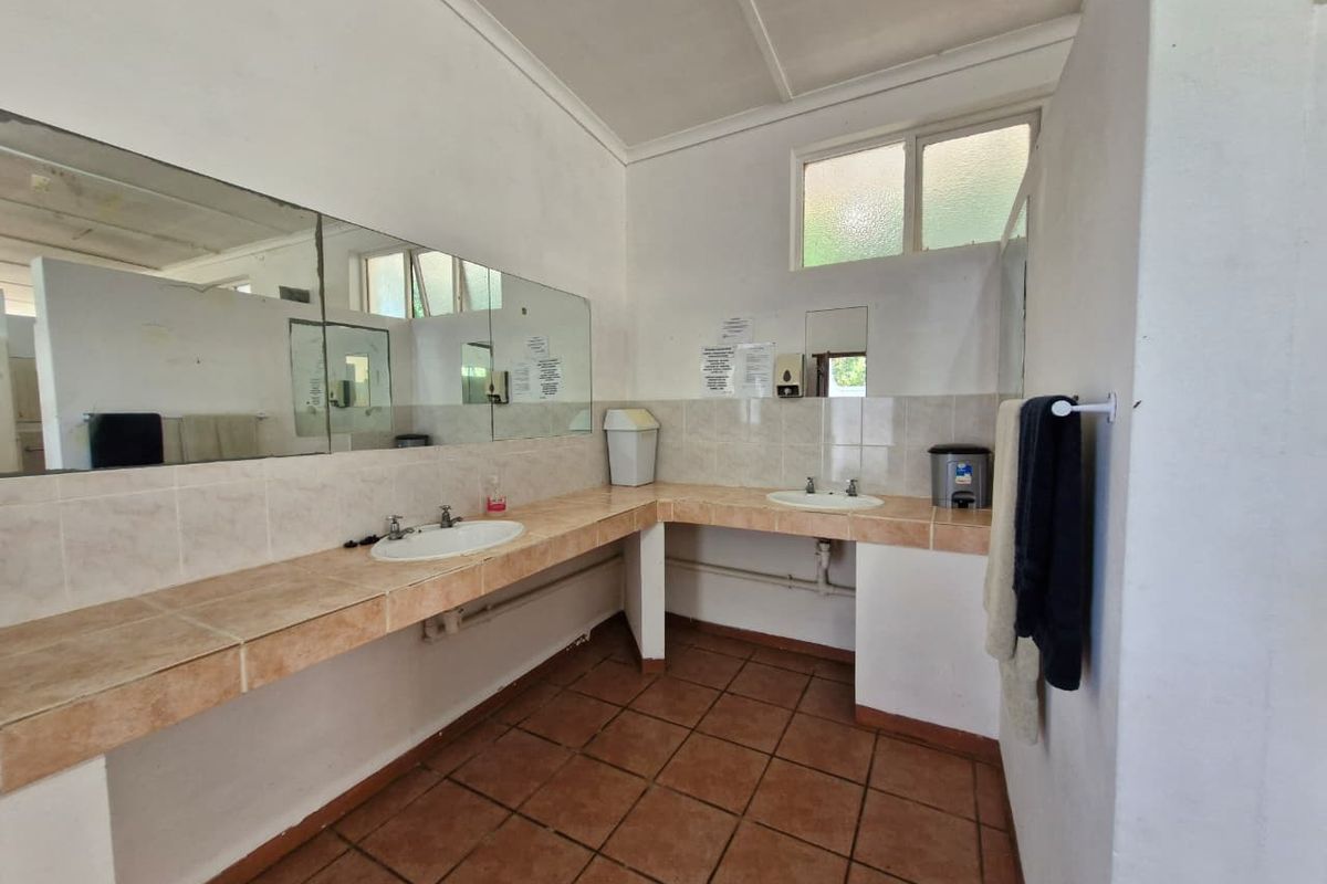 A functional, dated bathroom featuring a long tiled vanity with dual sinks, large wall mirrors, and ceramic floor tiles.
