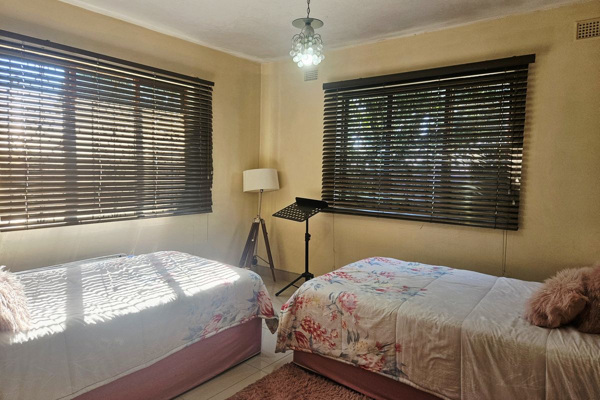 A bedroom featuring tiled flooring and dual windows with venetian blinds, requiring cosmetic updates to the wall finishes.