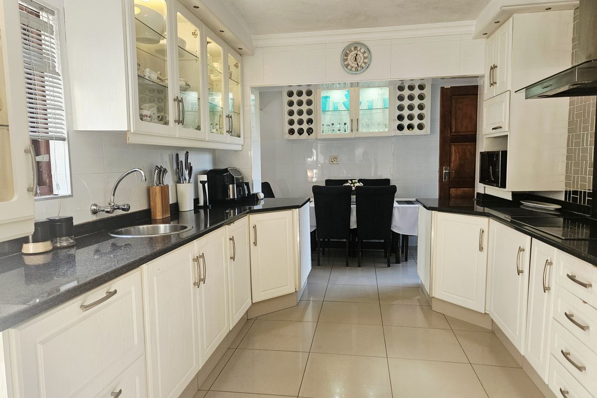 A well-maintained kitchen featuring white cabinetry, granite countertops, glass-front display units, and tiled flooring, offering a clean and functional workspace.