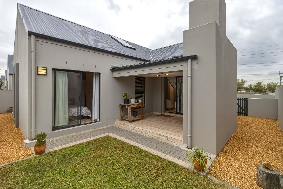 A well-maintained rear exterior featuring a covered patio, paved walkway, small lawn, and modern grey facade with a prominent chimney stack.
