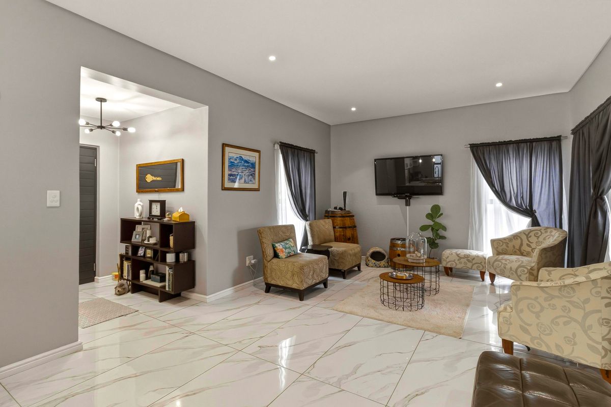 A bright and modern living room featuring polished marble-look floor tiles, recessed downlighting, and a seamless transition into the adjacent entryway.