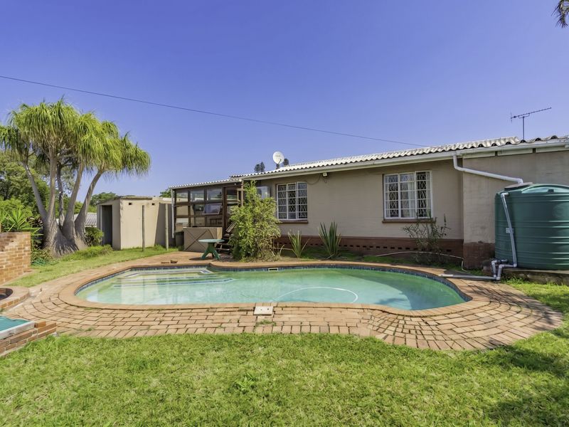 Rear garden area featuring a swimming pool, brick paving, built-in braai, and a water storage tank against the house exterior.