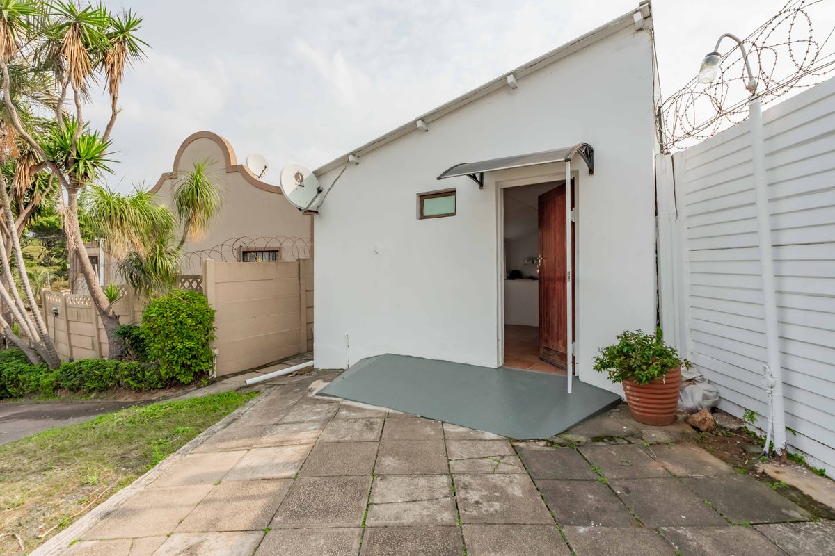 Rear exterior view of the property featuring a paved patio area, security fencing, and an entrance door with a protective awning.