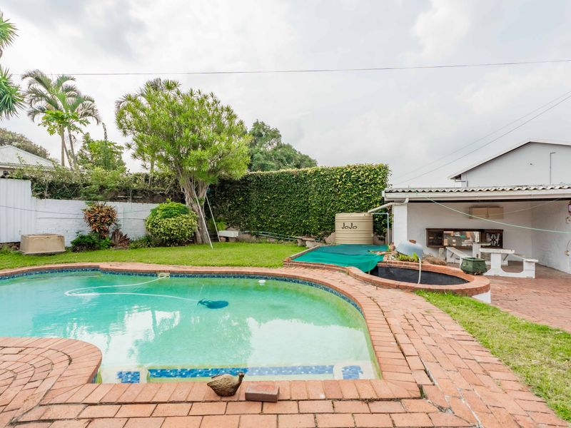 Outdoor pool area featuring a swimming pool with brick coping, a water tank, and an adjacent covered patio space with brick paving.