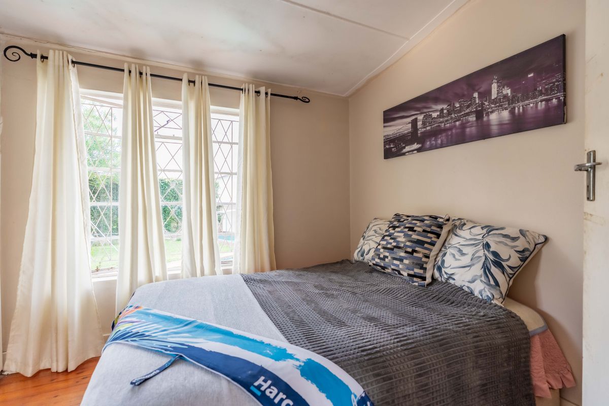 A cozy bedroom featuring timber flooring and a leaded glass window, offering a comfortable space with natural light.