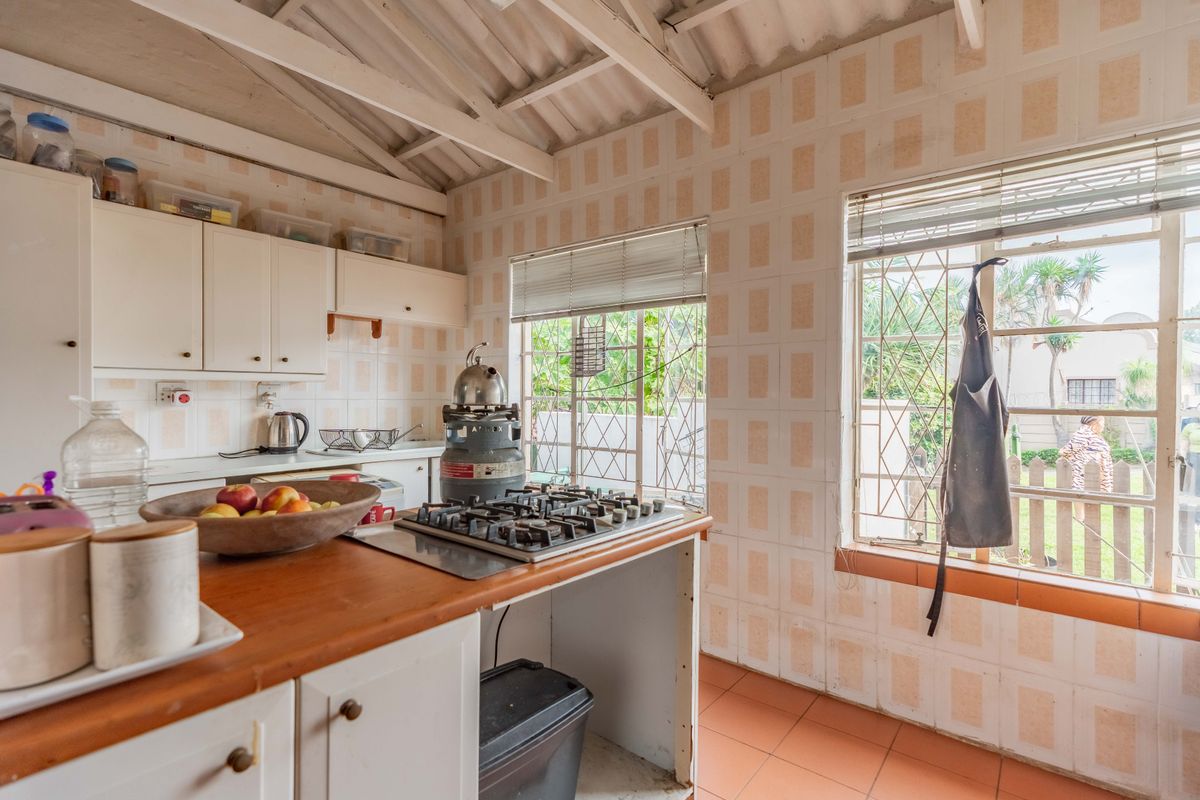 A dated kitchen featuring exposed timber rafters, tiled walls, and a gas hob, offering significant potential for a modern renovation.