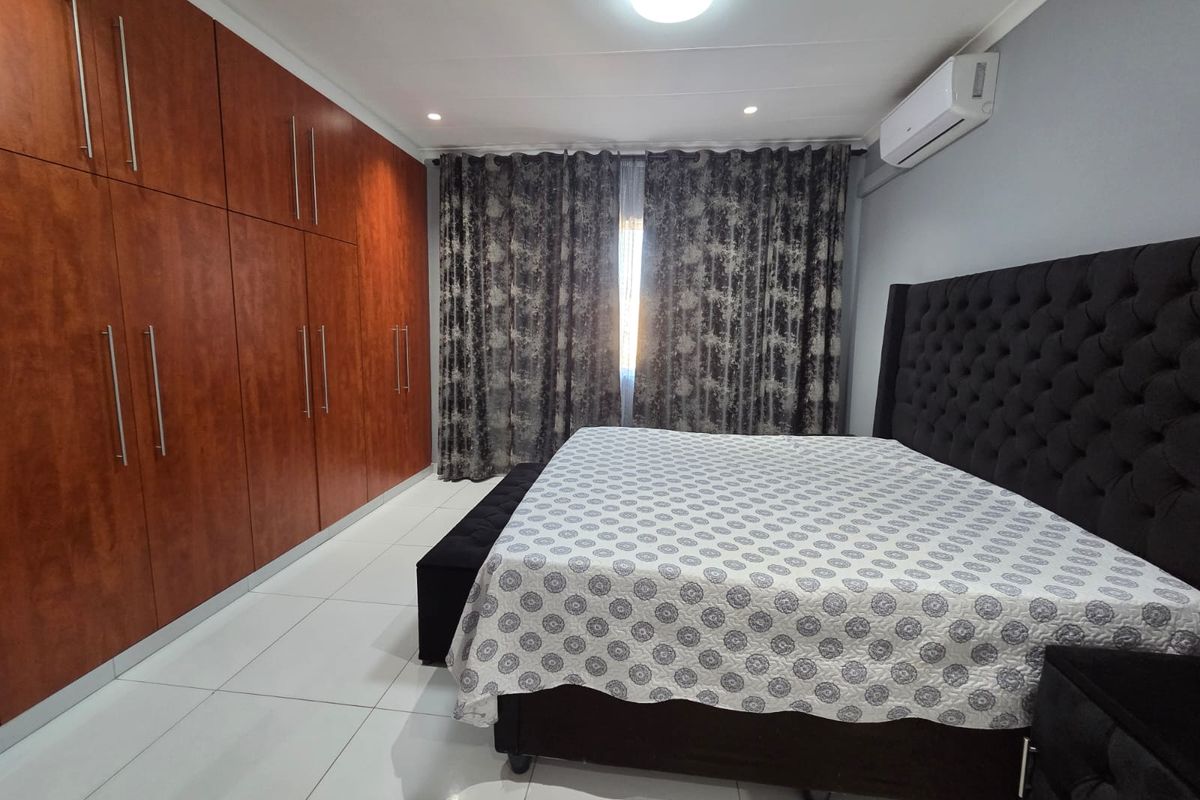 A well-maintained bedroom featuring extensive built-in wooden cupboards, tiled flooring, and a wall-mounted air conditioning unit.