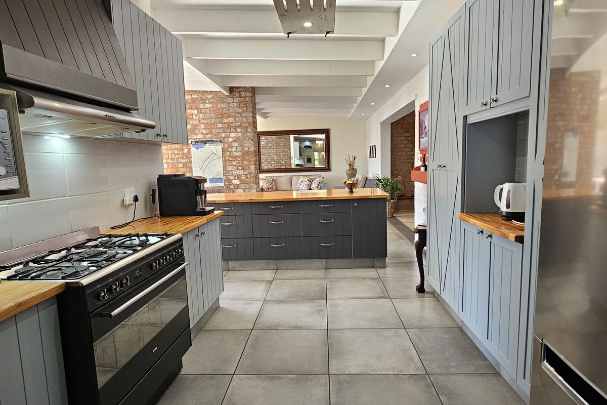 Modern kitchen featuring grey cabinetry, timber countertops, a gas range with extractor hood, and tiled flooring, flowing into an open-plan living area.