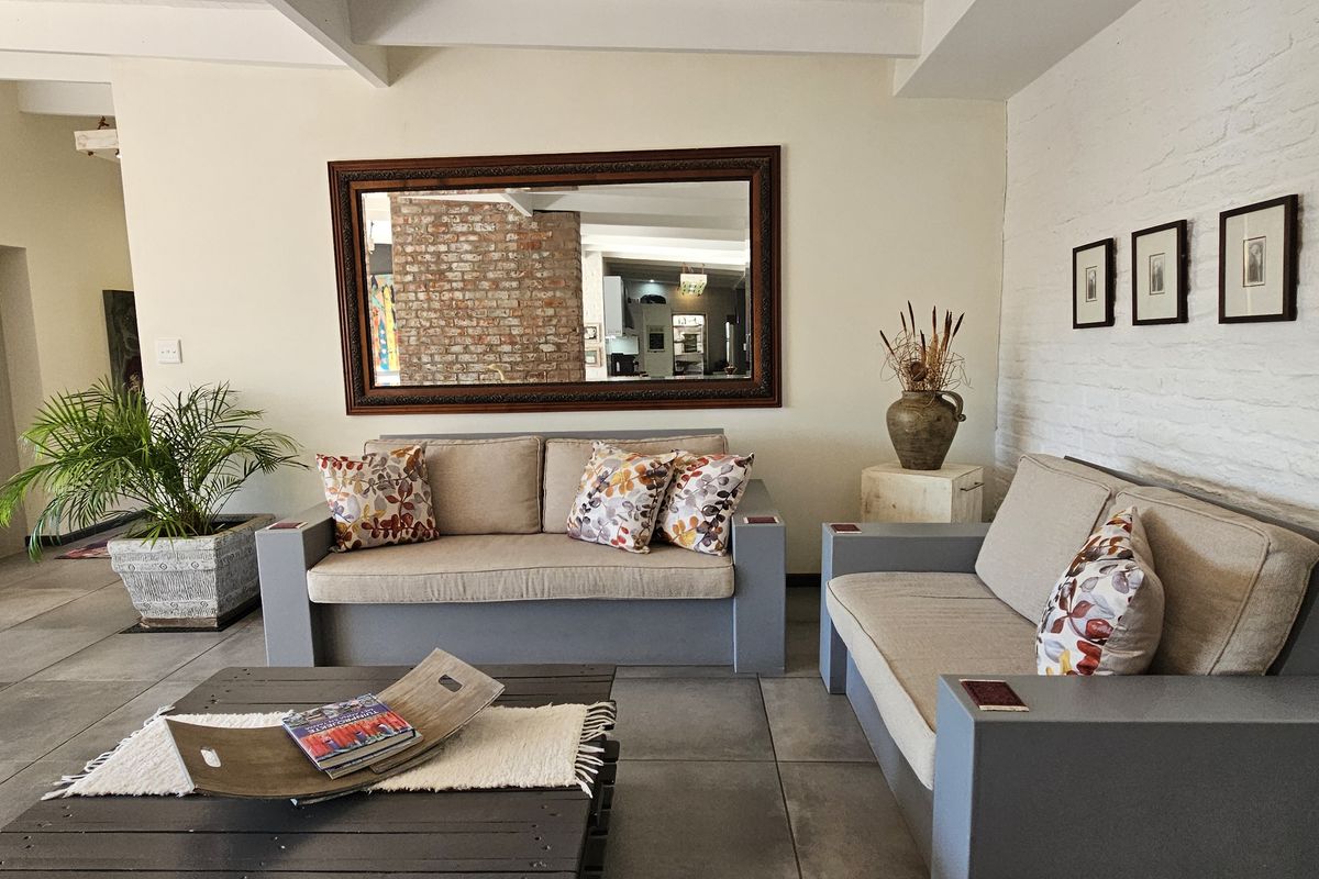 Spacious living area featuring exposed white-painted brick walls, large format floor tiles, and exposed ceiling beams.