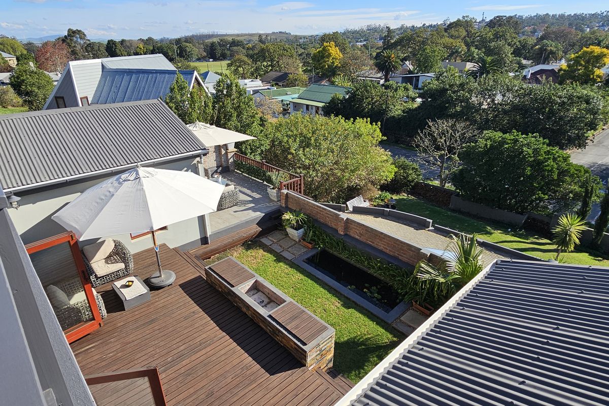 Elevated view of a landscaped rear garden featuring a timber deck, built-in fire pit, and a small water feature.